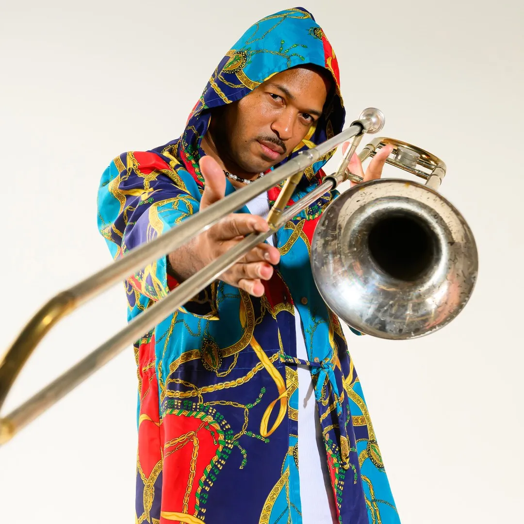 Trombonista com casaco estampado colorido e capuz tocando, sobre fundo branco