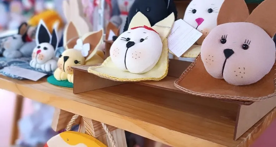 Bichos de pelúcia artesanais em forma de gato e coelho expostos sobre bancada de madeira