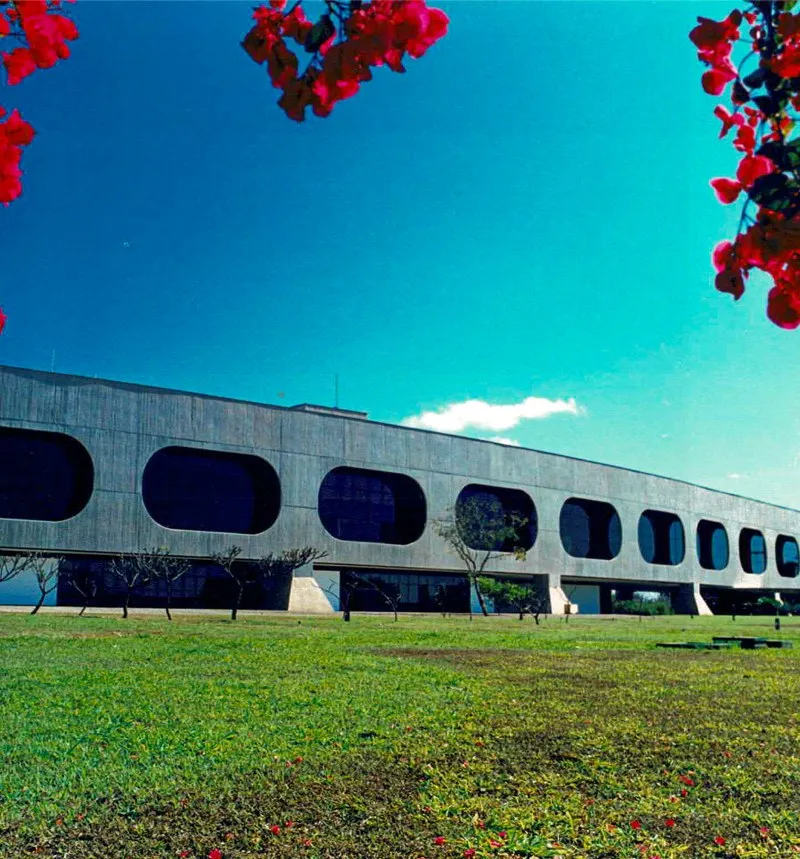 Fachada de concreto do CCBB Brasília com janelas ovais, gramado em primeiro plano e céu azul